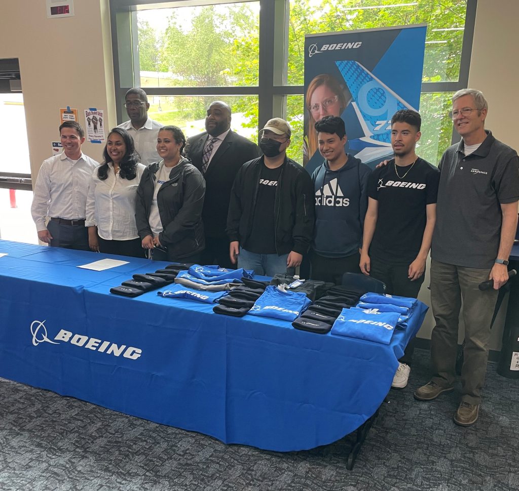Core Plus Aerospace students, teachers and Boeing leadership standing in front of a table after accepting a job offer from Boeing.