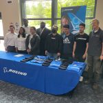 Core Plus Aerospace students, teachers and Boeing leadership standing in front of a table after accepting a job offer from Boeing.