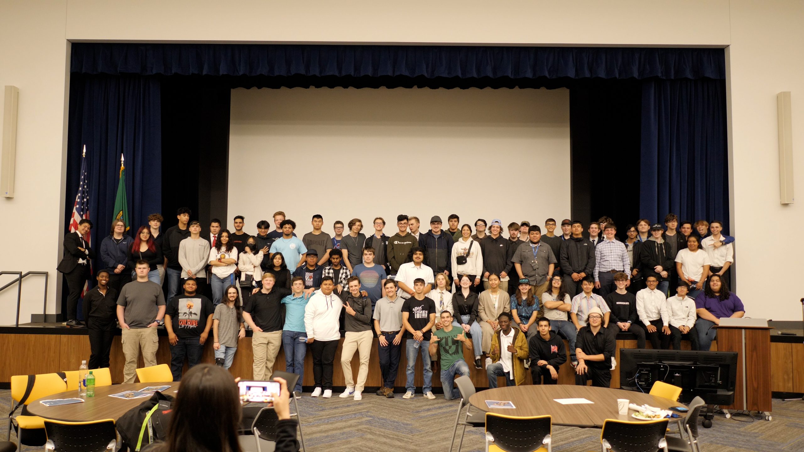 A group photo of 80 Core Plus Aerospace interns. The interns are standing on a stage. 