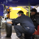 Two workers looking at a wheel under an airplane.