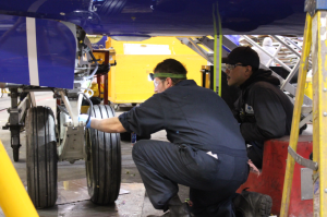 Two workers looking at a wheel under an airplane. 