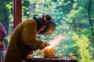 A student welding with trees in the background. 