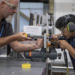 A student and an instructor working on a hands on project in a factory setting.